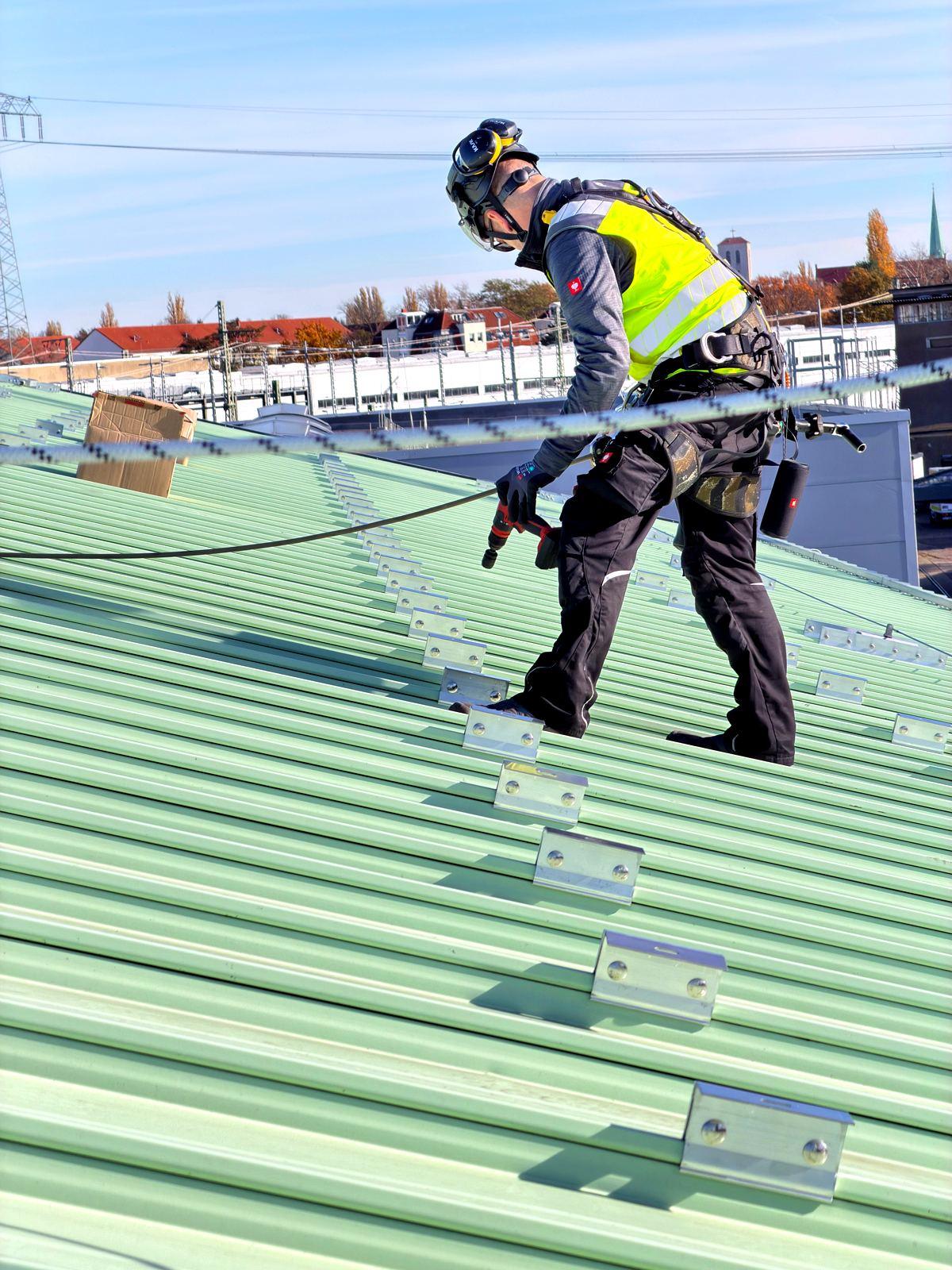 Höhenarbeiter bei der Montage der Halter für die Unterkonstruktion einer Photovoltaikanlage, gesichert an einem horizontalen Seilsicherungssystem