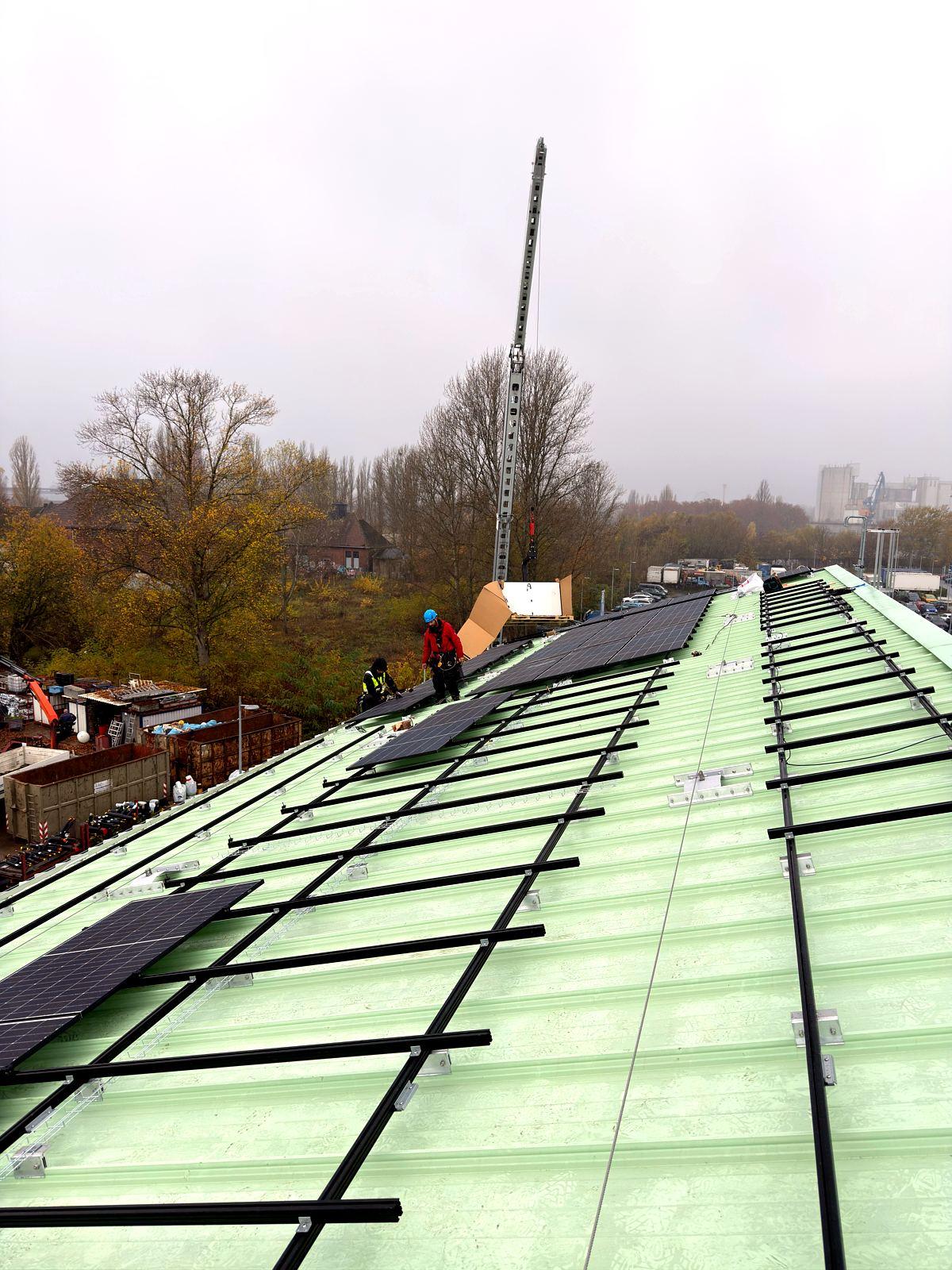 Übersicht der Montage einer Photovoltaikanlage auf einem langen Hallendach mit Höhenarbeitern